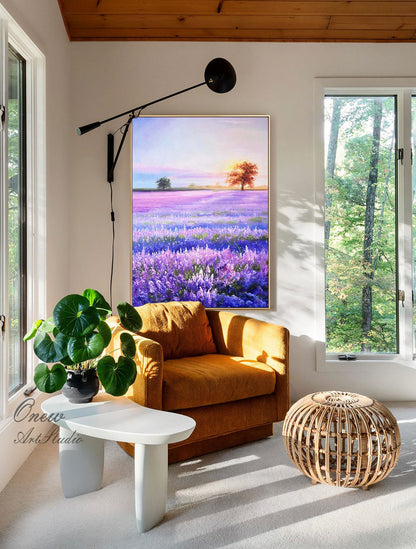 May include: A painting of a lavender field with a single tree in the distance. The painting is hanging on a wall in a living room with a brown armchair, a white side table, and a woven ottoman.