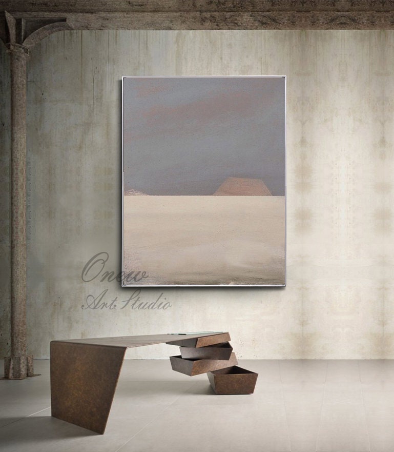 May include: Abstract painting with a gray and beige color scheme. The painting depicts a landscape with a horizon line and two hills in the distance. The painting is framed in a silver frame and is hanging on a concrete wall.