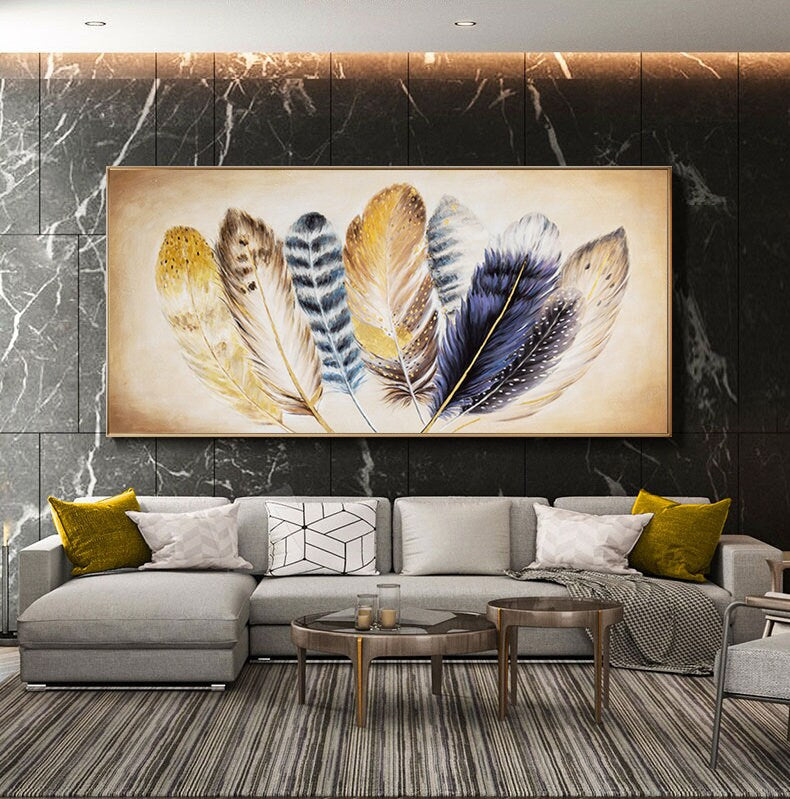 May include: A painting of a group of colorful feathers with gold accents on a white background. The painting is framed in a gold frame and is hanging on a wall.