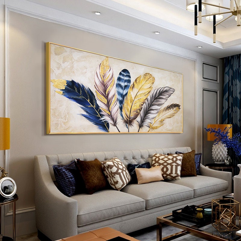 May include: A framed canvas painting featuring a cluster of stylized feathers in shades of gold, blue, and gray. The feathers are arranged in a fan-like pattern against a cream background.