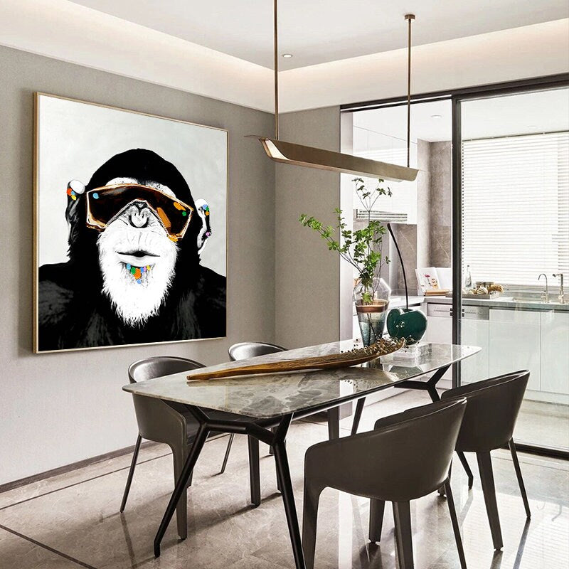 May include: A black and white painting of a monkey wearing sunglasses and a colorful beaded necklace. The painting is hanging on a wall in a dining room with a marble table and black chairs.