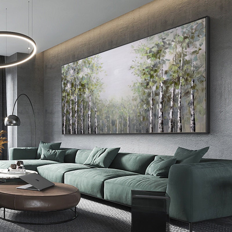 May include: A large abstract painting of a forest scene with white birch trees and green foliage. The painting is framed in a black frame and hangs on a wall in a modern living room.