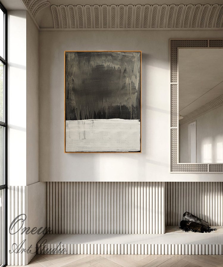 May include: Abstract painting with a dark gray and white color scheme. The painting is framed in a thin, gold frame and is hanging on a white wall in a modern interior.