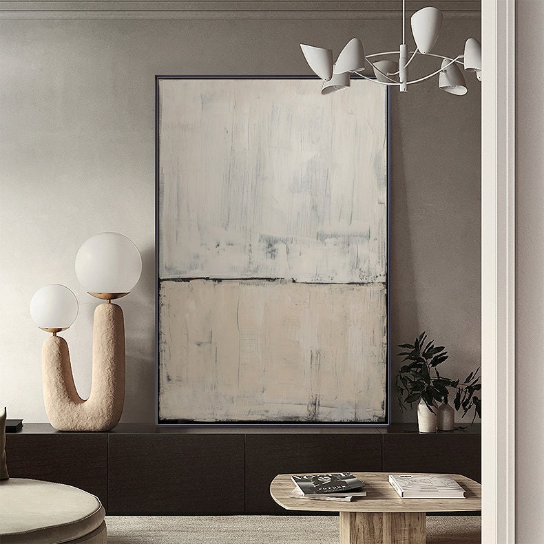 May include: Abstract painting with a horizontal line dividing the canvas into two sections. The top section is a light gray with white and blue brushstrokes. The bottom section is a light beige with white brushstrokes. The painting is framed in black.
