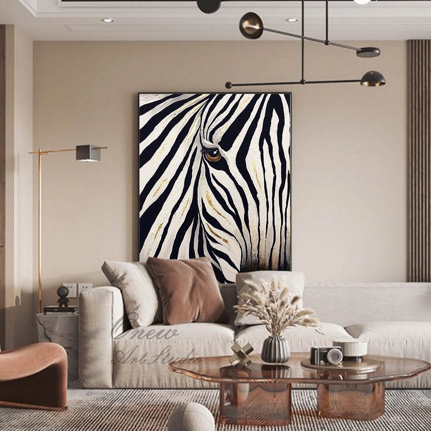 May include: A large framed canvas art piece featuring a close-up of a zebra's eye and face. The artwork has black and white stripes with gold accents. The painting is displayed in a living room setting.