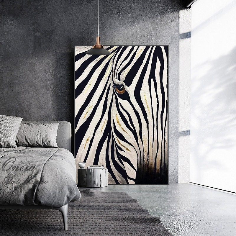 May include: A large canvas art print featuring a close-up of a zebra's face. The artwork showcases the animal's eye and distinctive black and white stripes, with gold accents. The painting is framed in black and hangs in a modern interior.