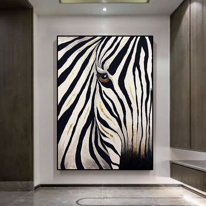 May include: A framed canvas art piece featuring a close-up of a zebra's face. The artwork showcases black and white stripes with gold accents, and a detailed brown eye. The painting is set against a neutral wall.
