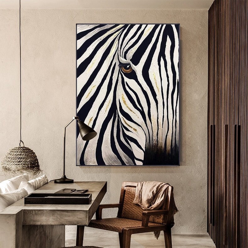 May include: A black and white zebra painting with gold accents. The artwork features a close-up of the zebra's face, with its eye visible. The painting is framed and hangs on a neutral-colored wall, adding a touch of wildlife to the room.