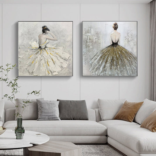 May include: Two square canvas paintings of a ballerina in a white and gold dress. The ballerina is facing away from the viewer in both paintings. The paintings are hung on a white wall above a white couch.
