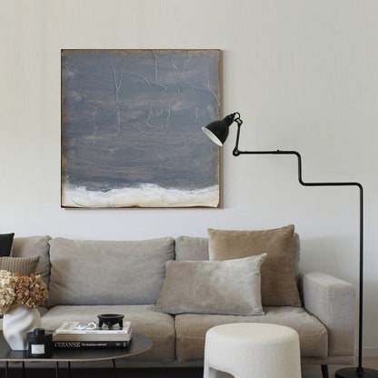 May include: A gray and white abstract painting hangs above a gray sofa with brown and beige pillows. A black floor lamp with a white shade is in the corner of the room.