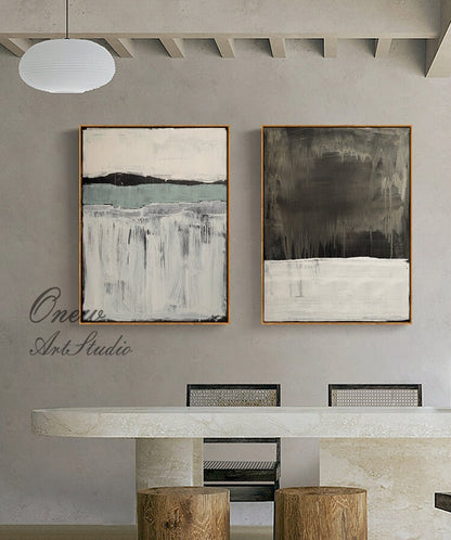 May include: Two abstract paintings with a white background and gray and blue brushstrokes. The paintings are framed in a light wood frame and are hanging on a gray wall.