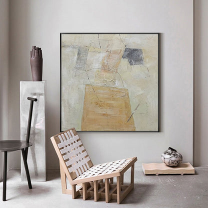 May include: Abstract painting with beige, white, and gray colors. The painting is framed in black and hangs on a white wall. A wooden chair with a white woven seat sits in front of the painting.