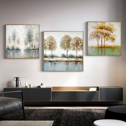 May include: Three framed abstract landscape paintings with a muted color palette of gold, brown, and blue. The paintings depict trees and water, with a focus on the reflection of the trees in the water. The paintings are hung on a white wall above a black entertainment center.