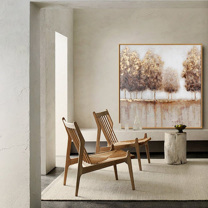 May include: Two wooden chairs with woven seats in a living room setting with a large abstract painting of trees in gold and brown tones on the wall.