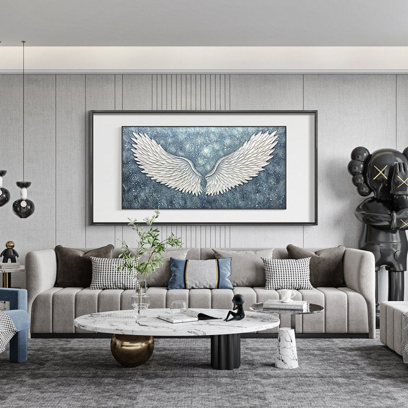 May include: A living room interior with a gray sofa, a white marble coffee table, and a large framed painting of white angel wings against a blue starry background.