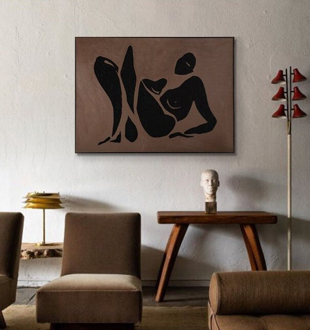 May include: A black and white abstract painting of a person reclining on a brown background. The painting is framed and hanging on a wall.