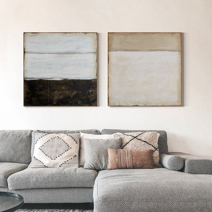 May include: Two abstract paintings with horizontal lines in shades of white, brown, and beige. The paintings are framed and hung on a white wall above a gray sectional sofa with pillows.