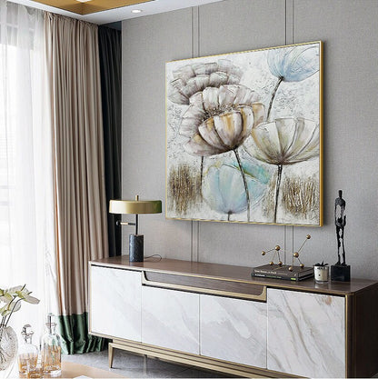 May include: A framed canvas painting with a textured, abstract floral design in shades of white, beige, and blue. The painting is set against a gray wall and a wooden cabinet with marble-like drawers.