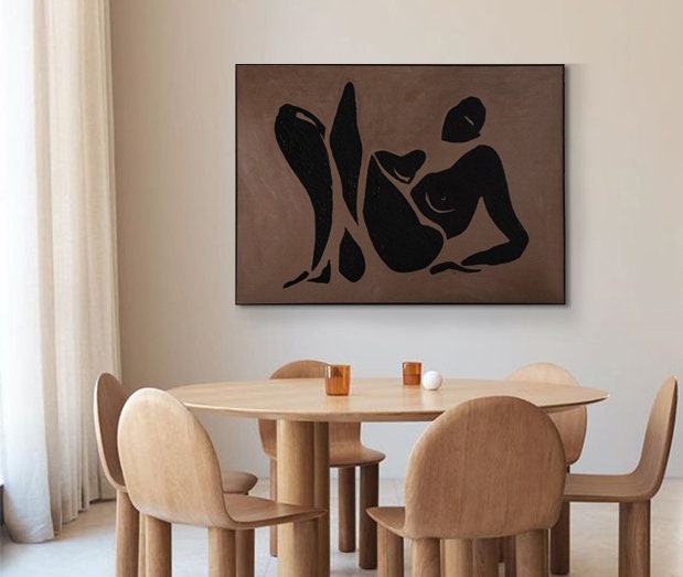 May include: A black and white abstract art print of a person reclining on a brown background. The print is framed and hanging on a wall in a room with a wooden table and chairs.