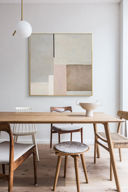 May include: A modern abstract painting with geometric shapes in shades of beige, brown, and pink hangs above a wooden dining table with chairs. The painting is framed in gold.