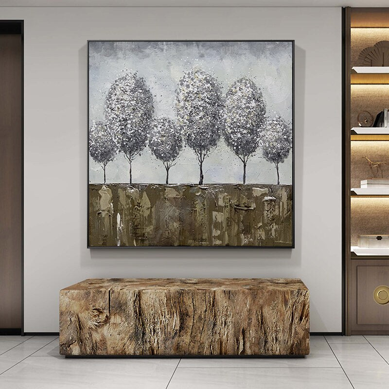 May include: A framed abstract painting of a row of five gray trees with white accents against a light blue background. The trees are set against a brown and gold textured background.