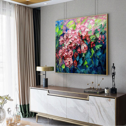 May include: A painting of a bouquet of pink roses with green leaves against a blue background. The painting is framed in gold and hanging on a gray wall.