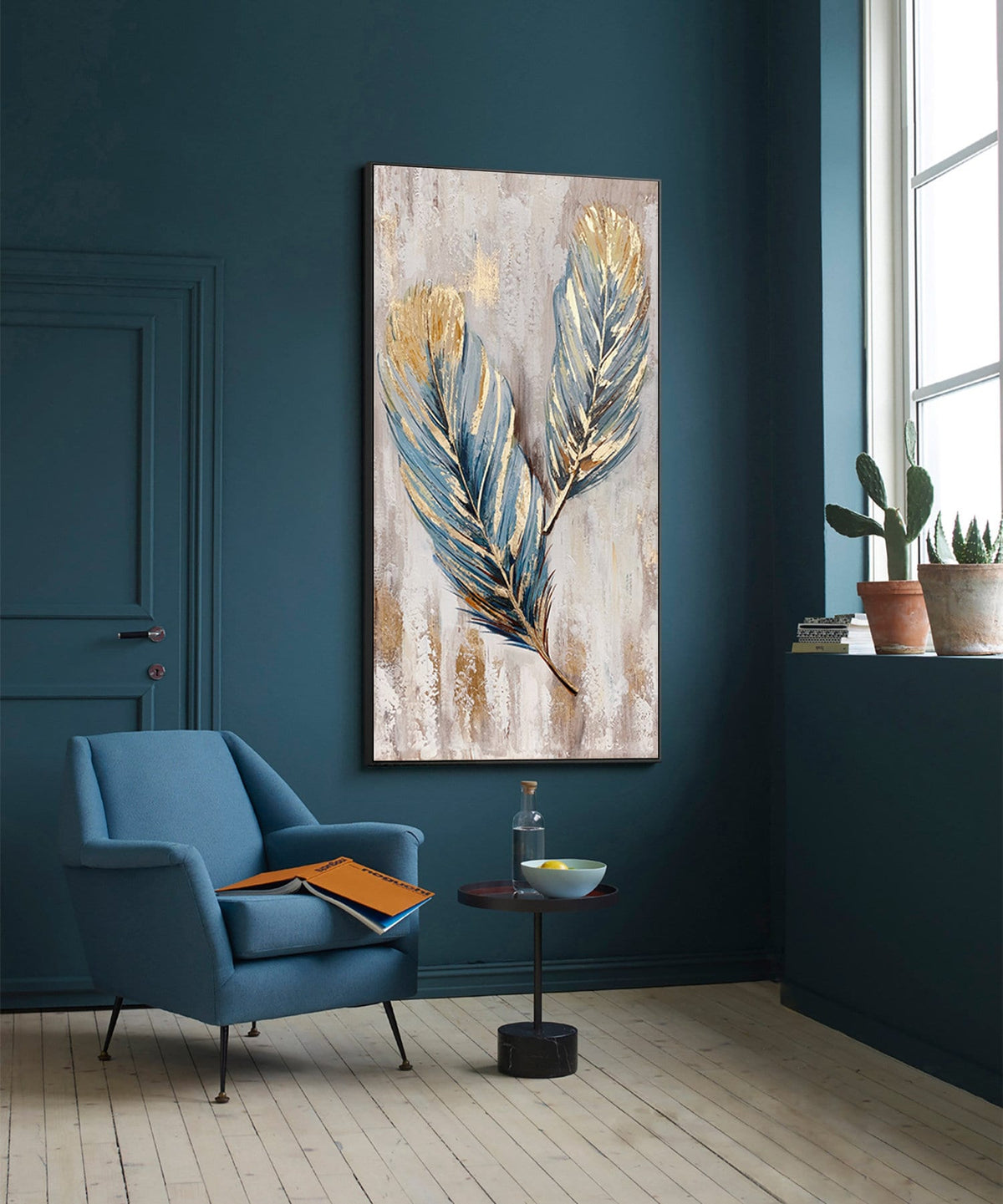 May include: A painting of two blue and gold feathers on a textured beige background. The painting is framed in a black frame and is hanging on a teal wall.