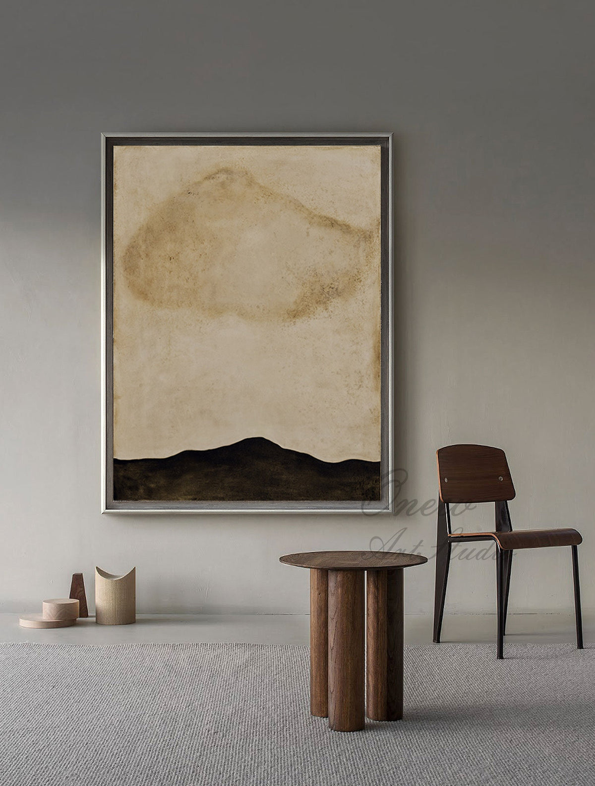 May include: Abstract painting in a silver frame with a brown and beige color scheme. The painting depicts a large brown cloud shape in the upper center of the canvas, with a dark brown mountain range at the bottom. The painting is hanging on a gray wall, with a wooden table and chair in the foreground.
