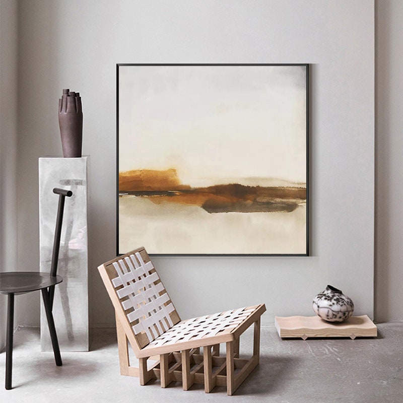 May include: Abstract landscape painting with brown and white tones. The painting is framed in black and hangs on a white wall. A wooden chair with a white woven seat sits in front of the painting.