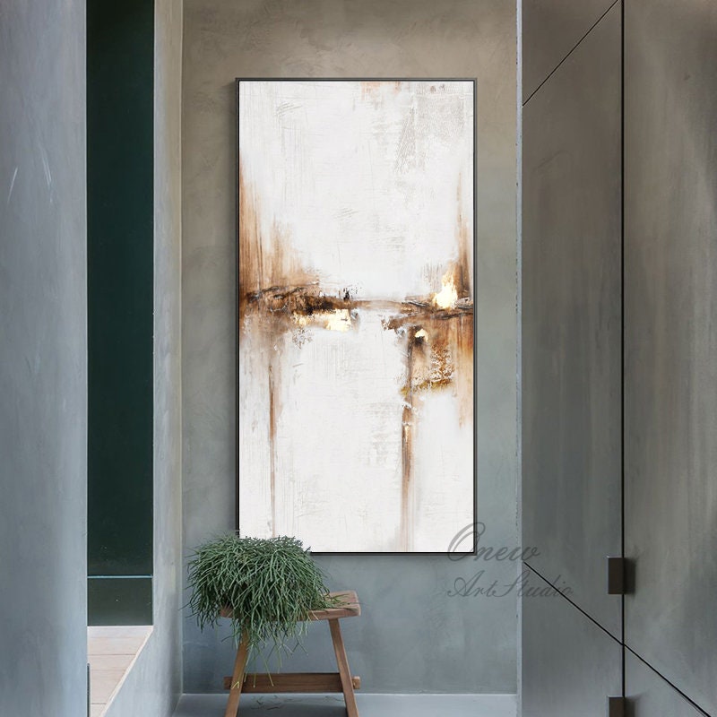 May include: Abstract painting with brown and gold accents on a white background. The painting is framed and hanging on a wall in a hallway.