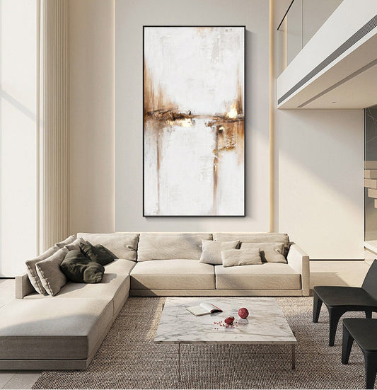 May include: Abstract painting with brown and white brushstrokes on a white canvas. The painting is framed in a black frame and is hanging on a white wall in a living room setting.