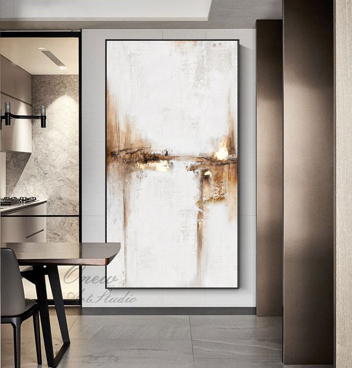 May include: Abstract painting with brown and white brushstrokes on a white canvas. The painting is hanging on a wall in a modern home.
