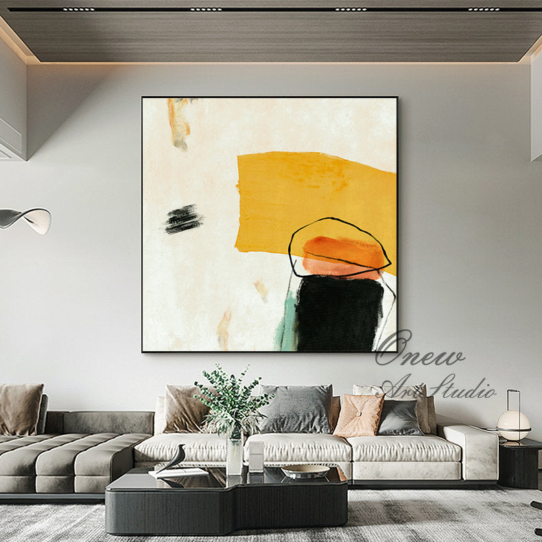 May include: Abstract painting with yellow, orange, black, and green shapes on a white background. The painting is framed in black and is hanging on a wall in a living room.