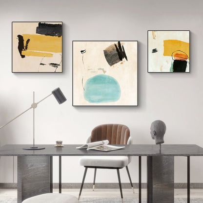 May include: Three abstract paintings with a minimalist style. The paintings feature geometric shapes and brushstrokes in shades of yellow, blue, black, and white. The paintings are hung on a white wall above a desk with a chair.