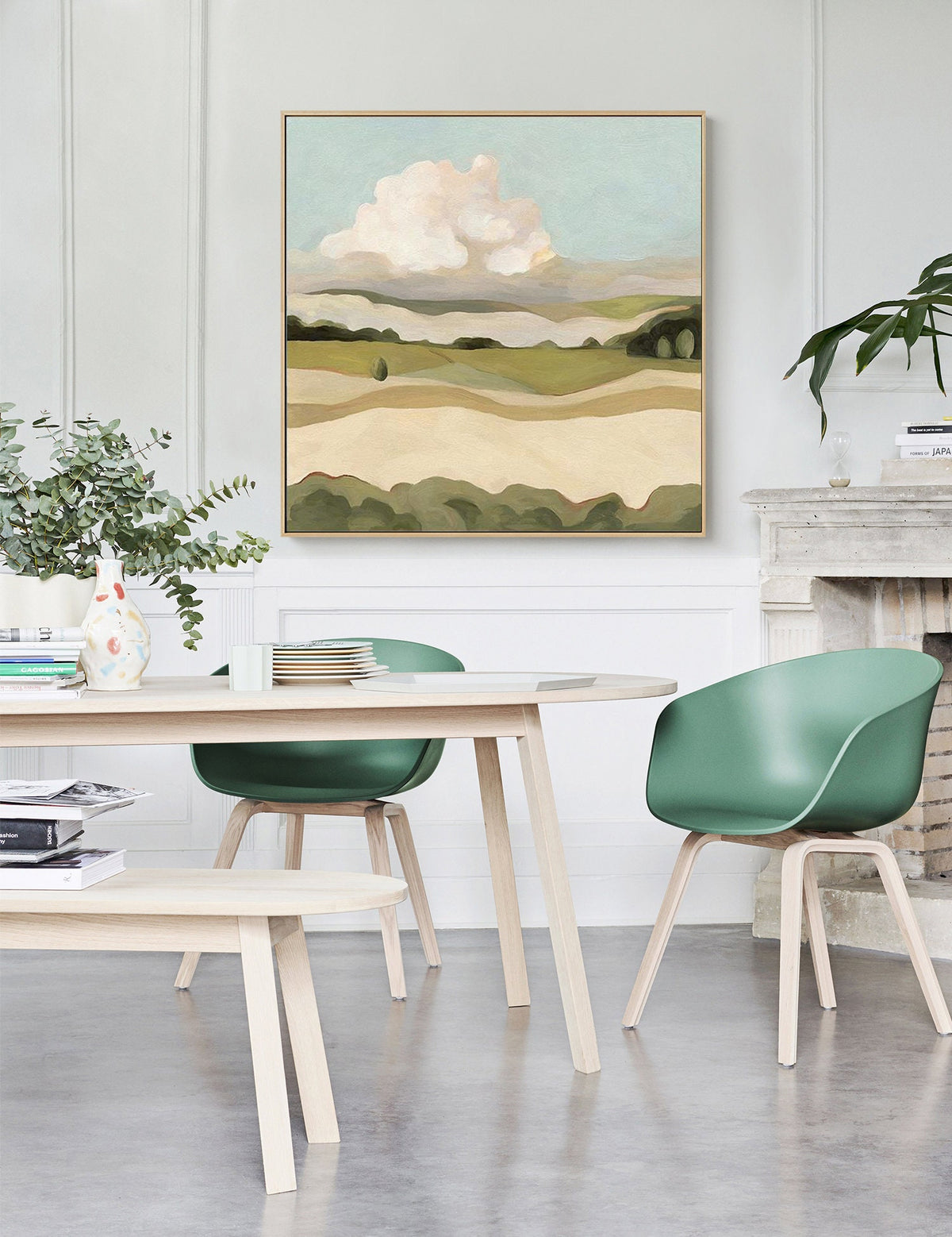 May include: A painting of a landscape with rolling hills, a large white cloud, and a blue sky. The painting is framed in a light wood frame and is hanging on a white wall.