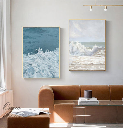 May include: Two abstract paintings of ocean waves. The painting on the left shows a close-up of white foamy waves against a blue background. The painting on the right shows a larger wave breaking on a sandy beach with a cloudy sky.