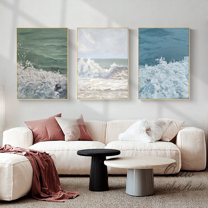 May include: Three framed canvas prints depicting abstract ocean waves in shades of blue, green, and white. The prints are hung on a white wall above a white couch with pillows.