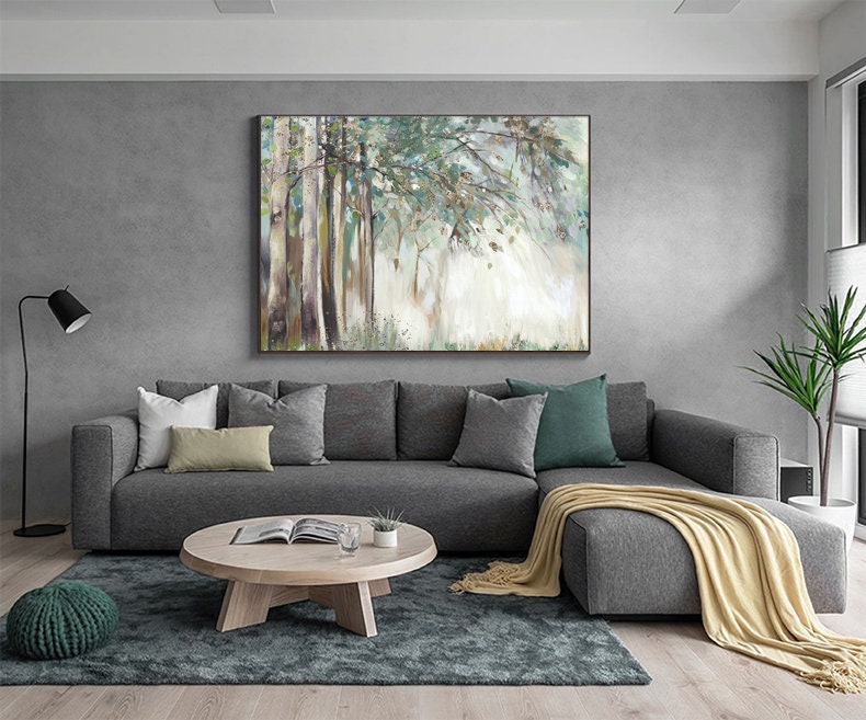 May include: A gray sectional sofa with a light beige throw blanket, a wooden coffee table, and a green throw pillow. A large abstract painting of a forest scene hangs on the wall behind the sofa.