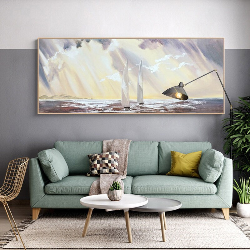 May include: A painting of two sailboats on a body of water with a cloudy sky and sunbeams. The painting is framed and hanging on a wall above a green sofa with pillows.