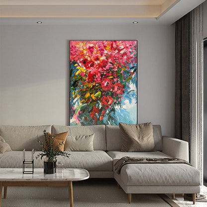 May include: A large abstract painting of a bouquet of pink, red, and yellow flowers with green leaves against a blue background. The painting is hanging on a wall in a living room with a gray sectional sofa and a coffee table.