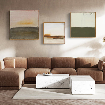 May include: Three abstract landscape paintings with muted colors in gold frames hanging on a beige wall above a brown sectional sofa and two white marble coffee tables.