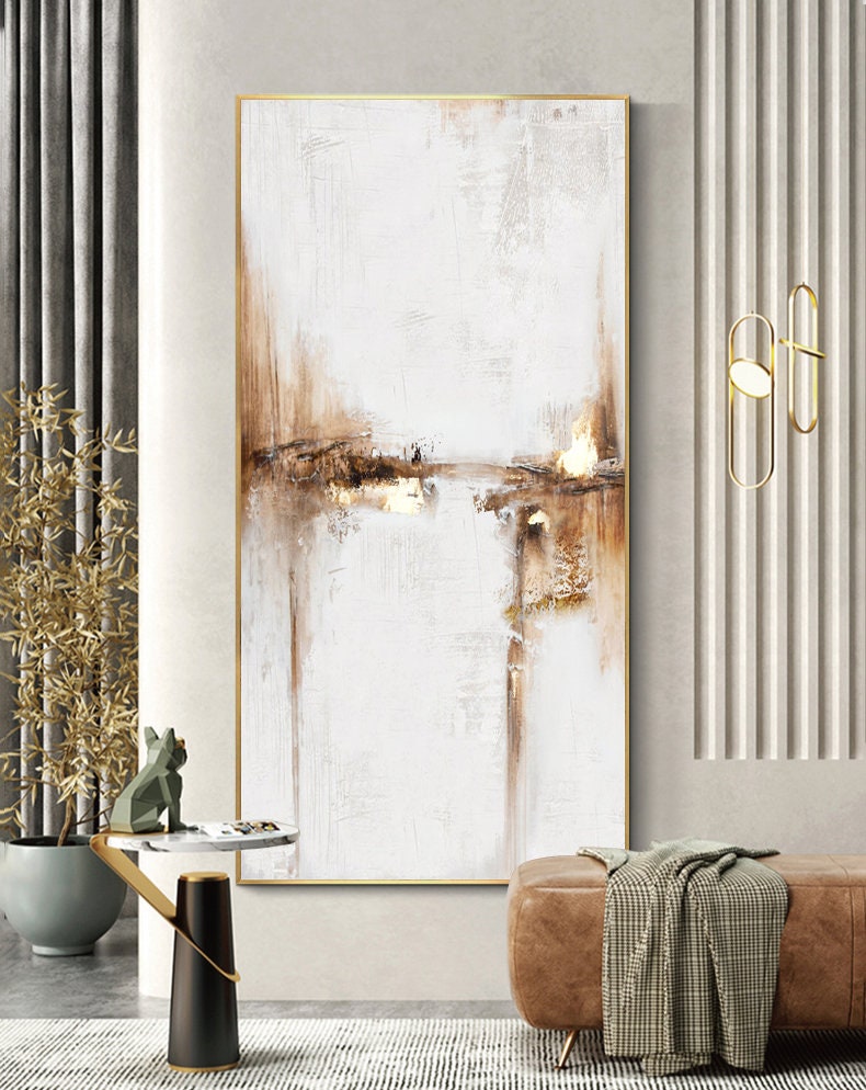 May include: Abstract landscape painting with brown and gold accents on a white background. The painting is framed in gold and hangs on a white wall.