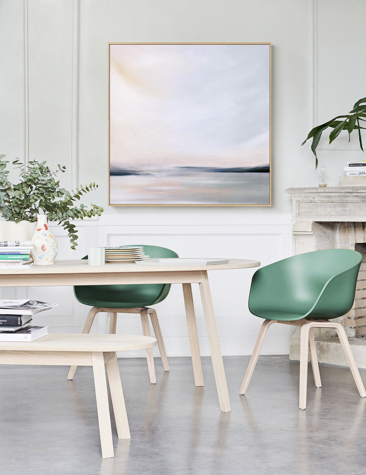 May include: A light wood dining table with a light wood bench and four green chairs. A painting of a landscape with a light blue sky and a horizon line is hanging on the wall behind the table.