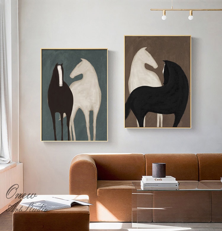 May include: Two abstract paintings of horses in black and white. The paintings are framed in gold and hung on a white wall. The painting on the left has a blue background and the painting on the right has a brown background.