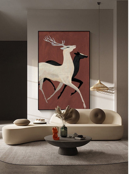May include: A framed painting of two deer running on a red background. The deer are white and black, and the painting is hanging on a wall in a living room setting.