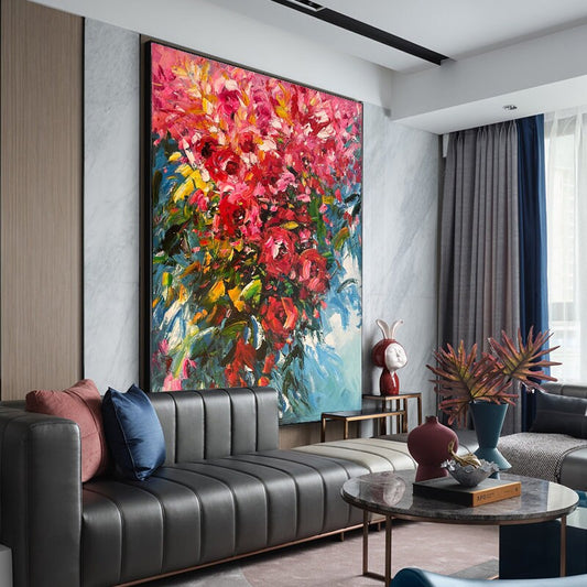 May include: A large abstract painting of a bouquet of pink flowers with green leaves against a blue background. The painting is hanging on a wall in a living room with a black leather sofa, a coffee table, and a vase with a plant.