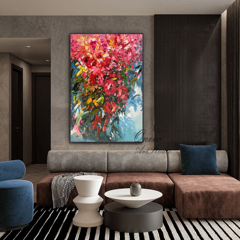 May include: A large abstract painting of a bouquet of pink flowers with green leaves against a blue and white background. The painting is framed and hanging on a wall in a living room.