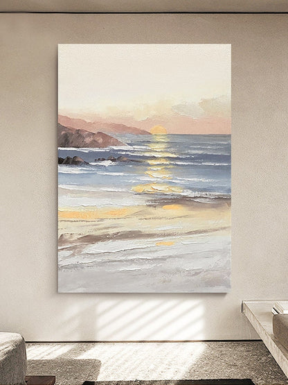 May include: A painting of a seascape with a sunset over the ocean. The sky is a soft pink and orange, and the water is a light blue. The waves are crashing on the shore, and there are some rocks in the foreground.