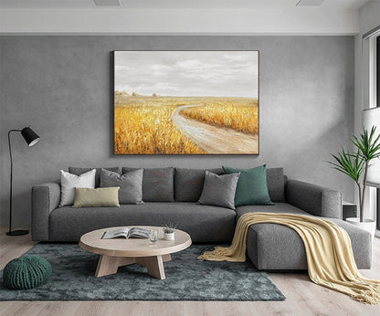 May include: A gray sectional sofa with a throw blanket, a coffee table, and a floor lamp in a living room. A painting of a dirt road leading through a field of golden wheat hangs on the wall.