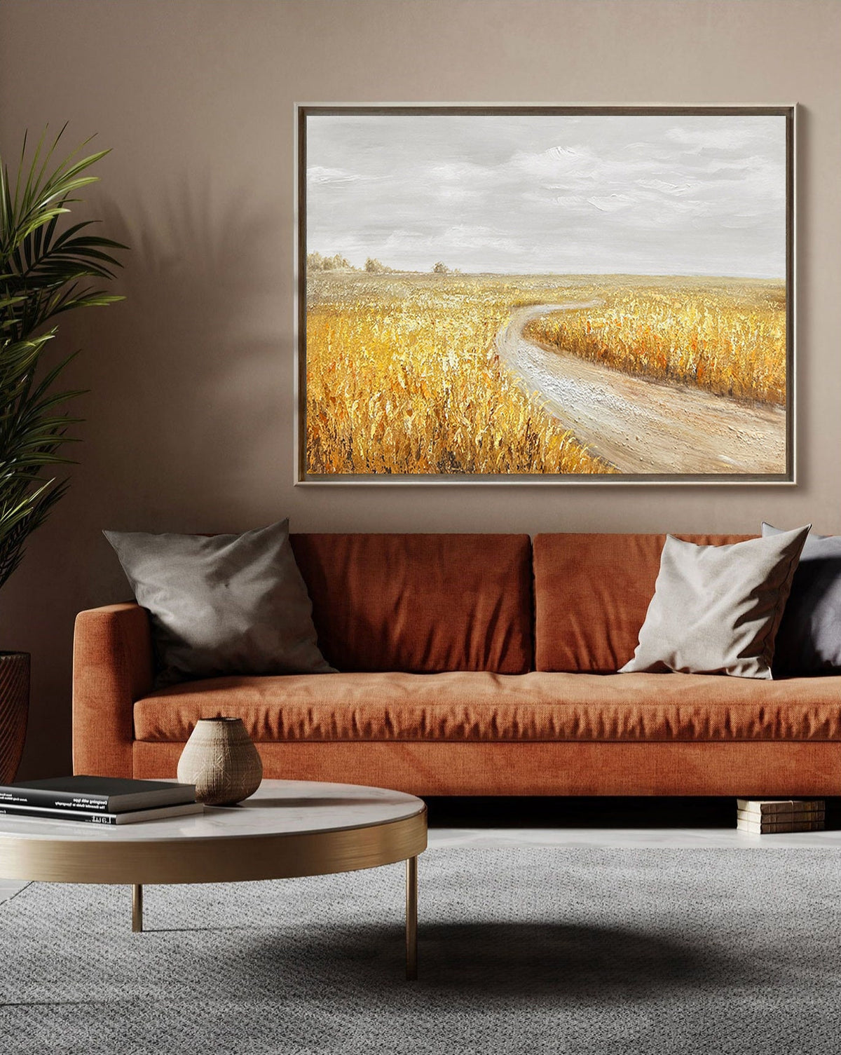 May include: A painting of a winding dirt road leading through a field of golden wheat. The sky is a light gray with a few clouds. The painting is framed in a simple, gold frame.